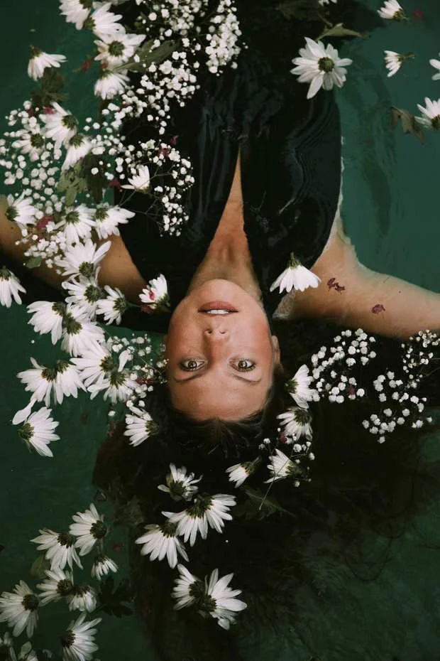 Una persona flota en el agua rodeada de flores blancas.